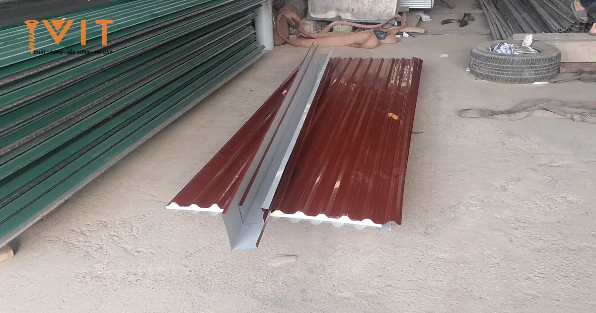 Hai tấm tôn xốp cách nhiệt màu đỏ và một máng tôn đặt trên nền xưởng, bên cạnh chồng tôn xốp màu xanh