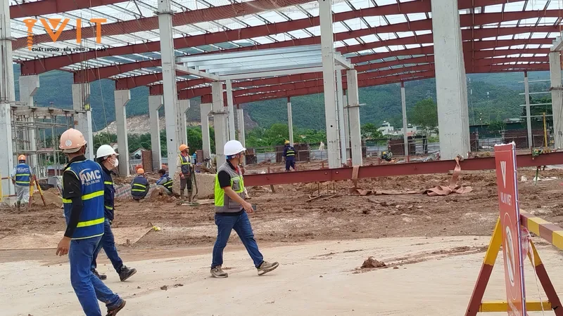 Kỹ sư và công nhân đội mũ bảo hộ trên công trường nhà xưởng khung thép đang dựng kèo mái