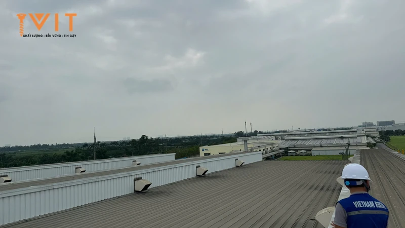 Người đội mũ bảo hộ khảo sát mái tôn nhà xưởng rộng có dãy chụp thông gió trên mái