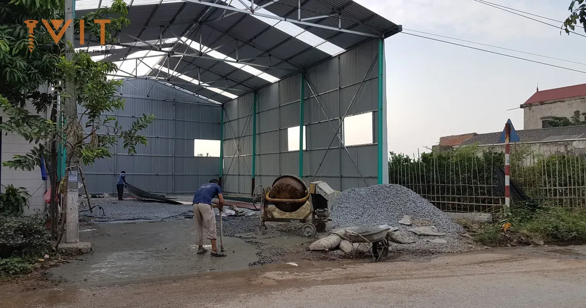 Nhà xưởng tiền chế khung thép đã lợp mái và vách tôn, thợ đang đổ nền bê tông phía trước