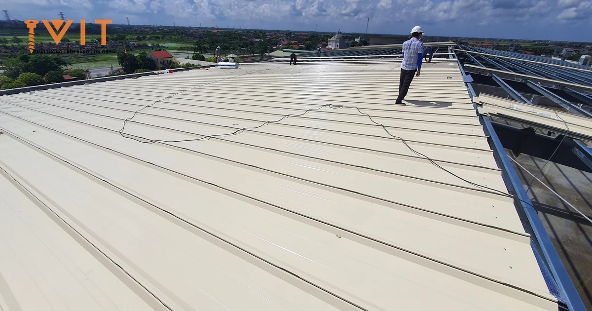 Thợ đi trên mái tôn nhà xưởng đang lợp, bên cạnh là khung xà gồ chưa phủ tôn