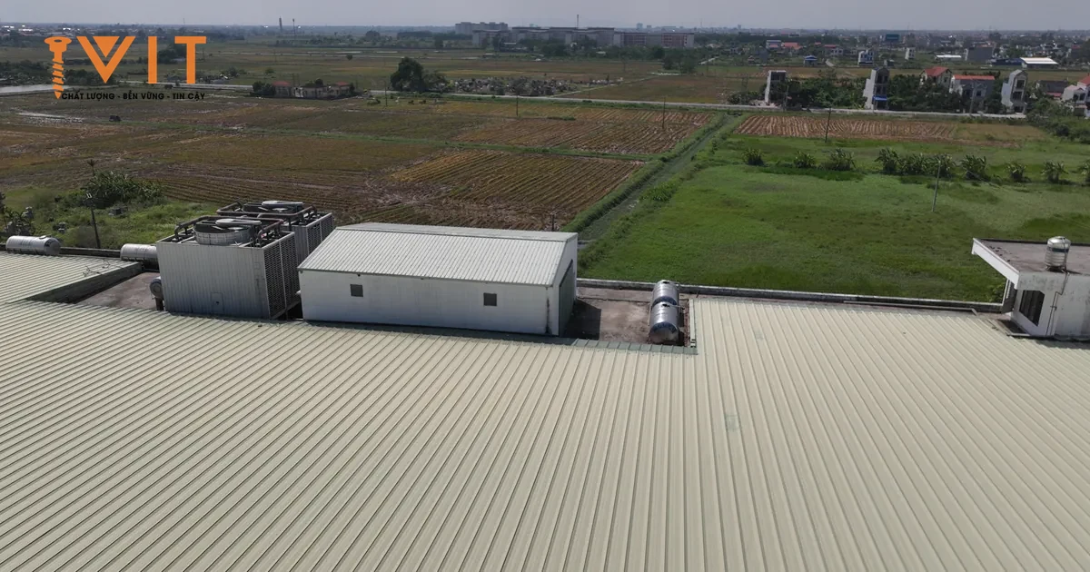 Mái tôn gân đứng phủ kín nhà xưởng lớn nhìn từ trên cao, phía xa là cánh đồng