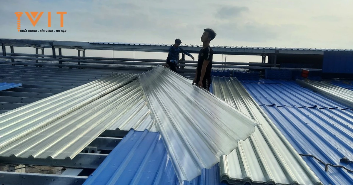 Thợ trải tấm lấy sáng polycarbonate dạng sóng xen giữa các tấm tôn xanh trên mái nhà xưởng