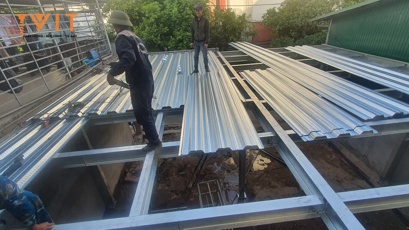 Thợ xếp các tấm thép mạ màu bạc chưa sơn lên khung thép, bề mặt lớp mạ kim loại lộ rõ
