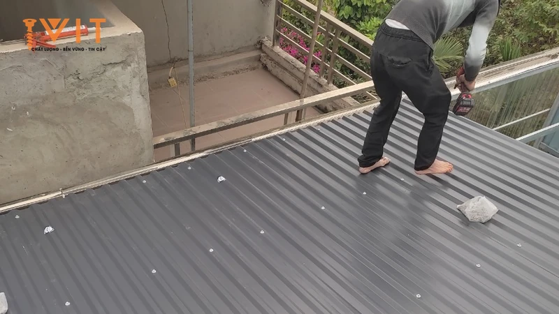Thợ bắn vít trên mái tôn sóng màu xám, các đầu vít đã bắt lộ trên mặt tôn