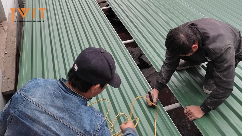 Hai thợ căng dây canh hàng trên tấm tôn lợp mái màu xanh trước khi bắn vít
