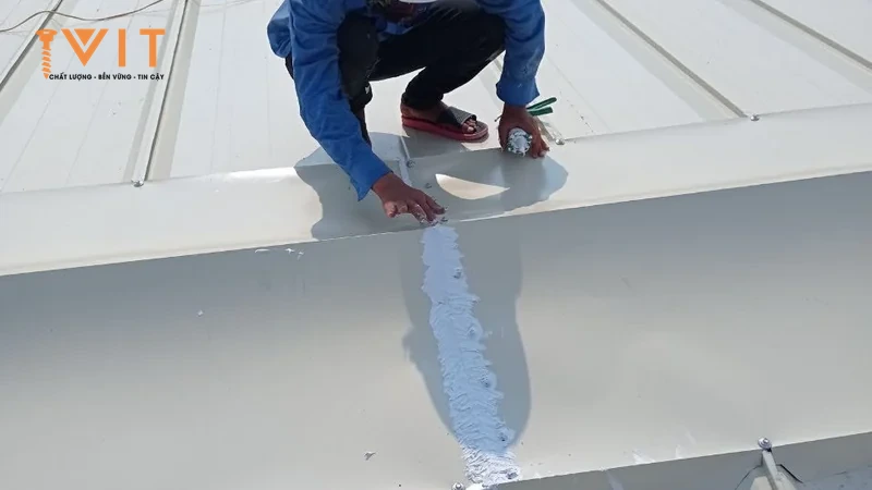 Thợ trám keo mối nối ngang giữa hai tấm trên mái tôn gân đứng màu trắng