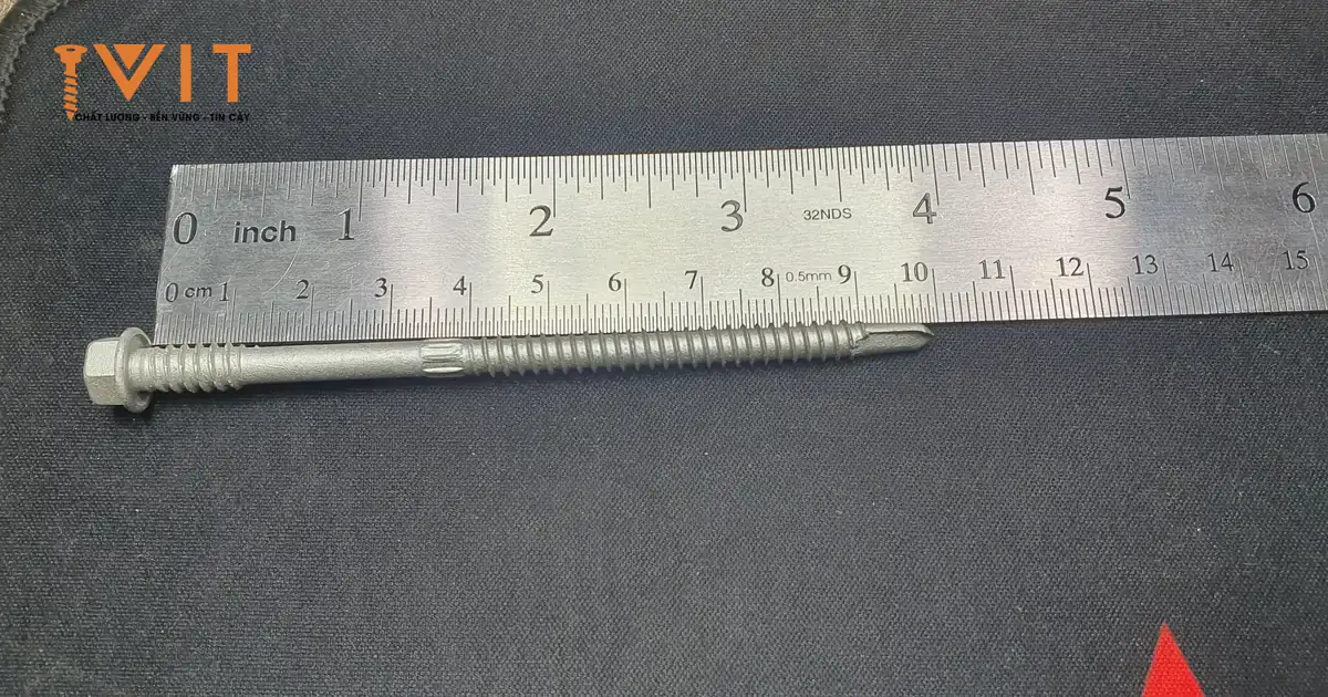 Vít bắn tôn panel ren kép Sheh Fung dài khoảng 100 mm, có đoạn khía giữa thân, đặt cạnh thước, chưa lắp long đệm